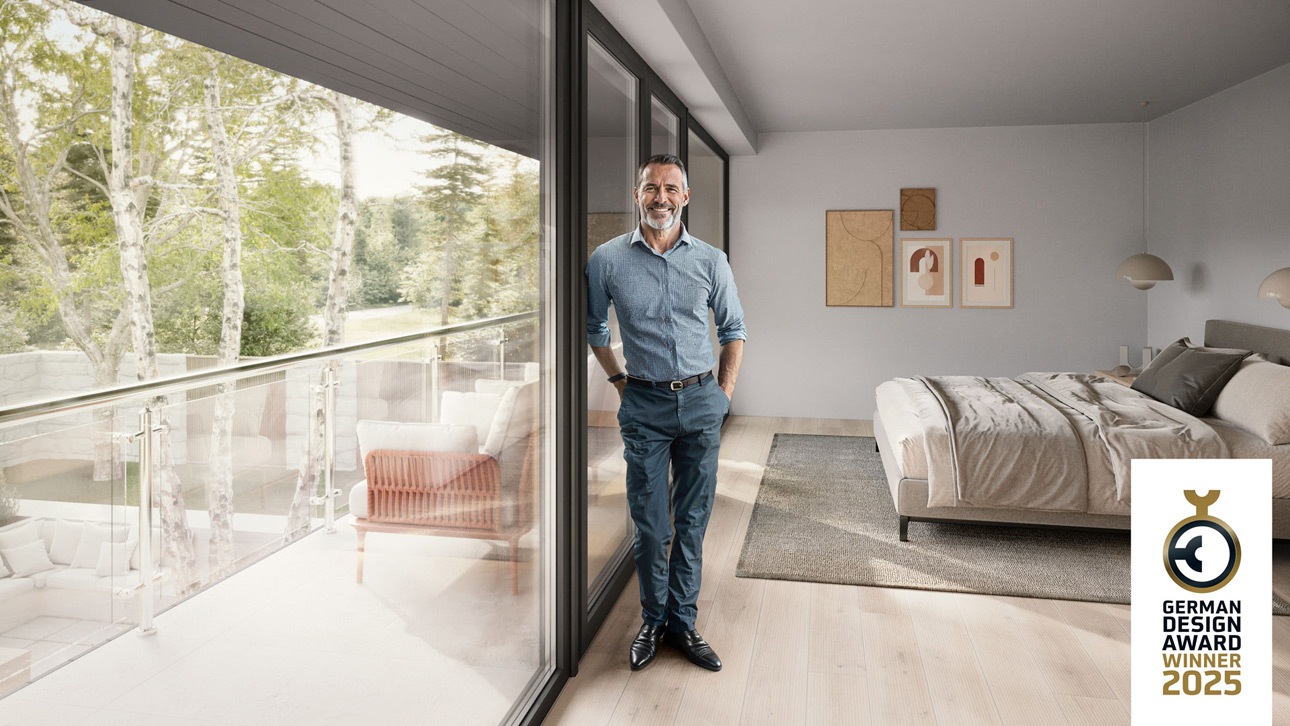 Ein lächelnder Mann steht vor einer Fensterfront - REHAU ARTEVO TERRA nachhaltige Fenster